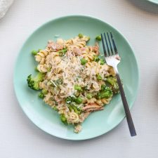 Creamy Homemade Tuna Helper on a green place topped with peas, broccoli and cheese. surrounded by bowls of peas, broccoli and cheese