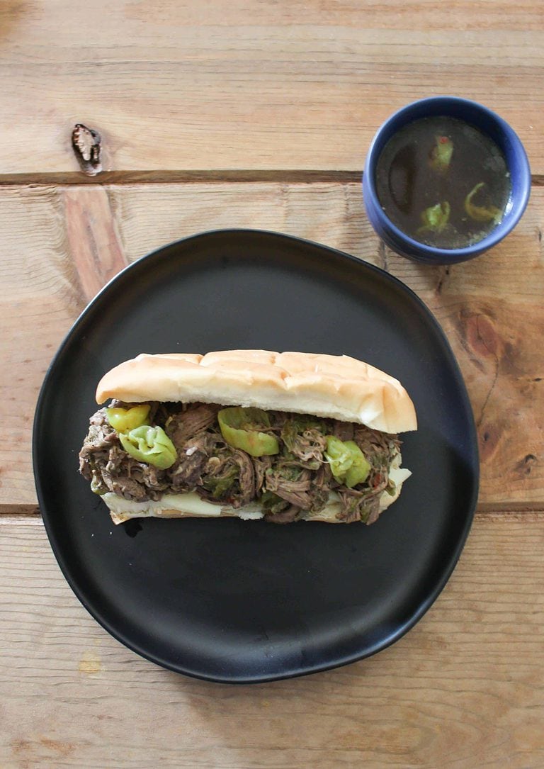 Italian Beef Sandwiches on a black plate, next to a small dish of broth.