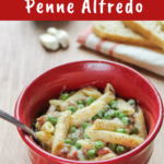 Prosciutto & Pea Alfredo with Penne in a red bowl. Bread and peas are behind it.