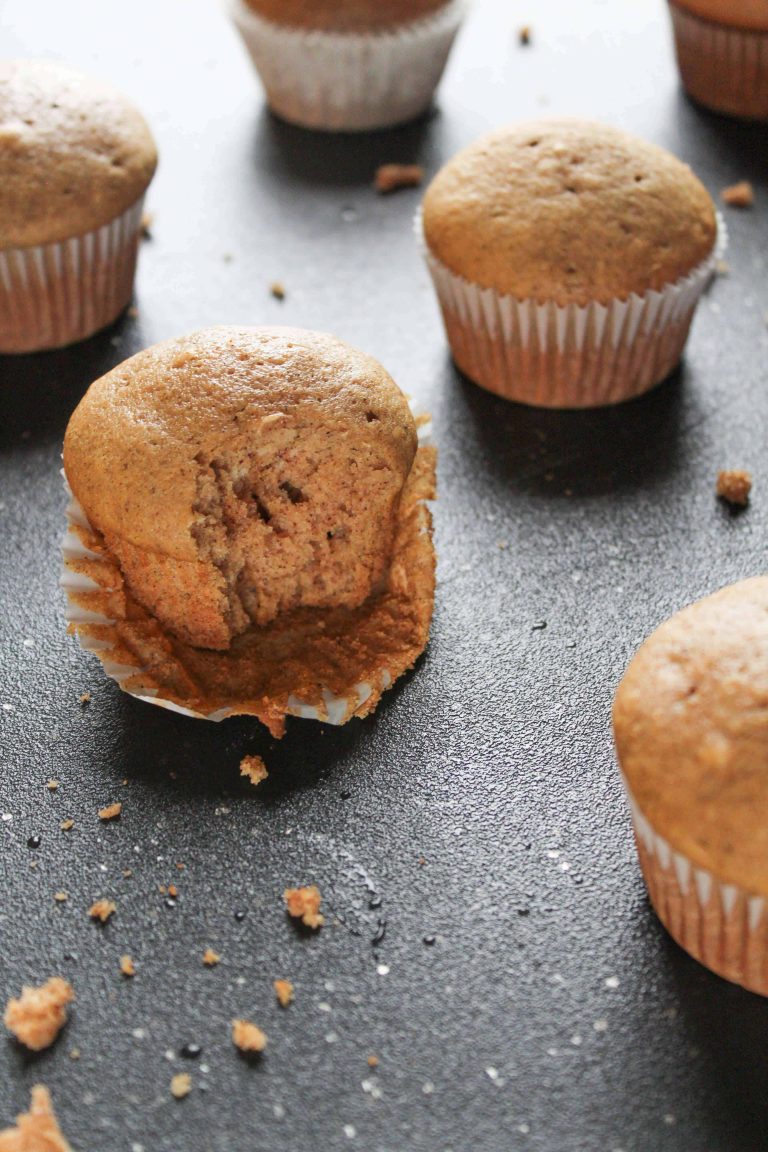 Chai tea muffins, one with a bit taken out of it, on a black surface