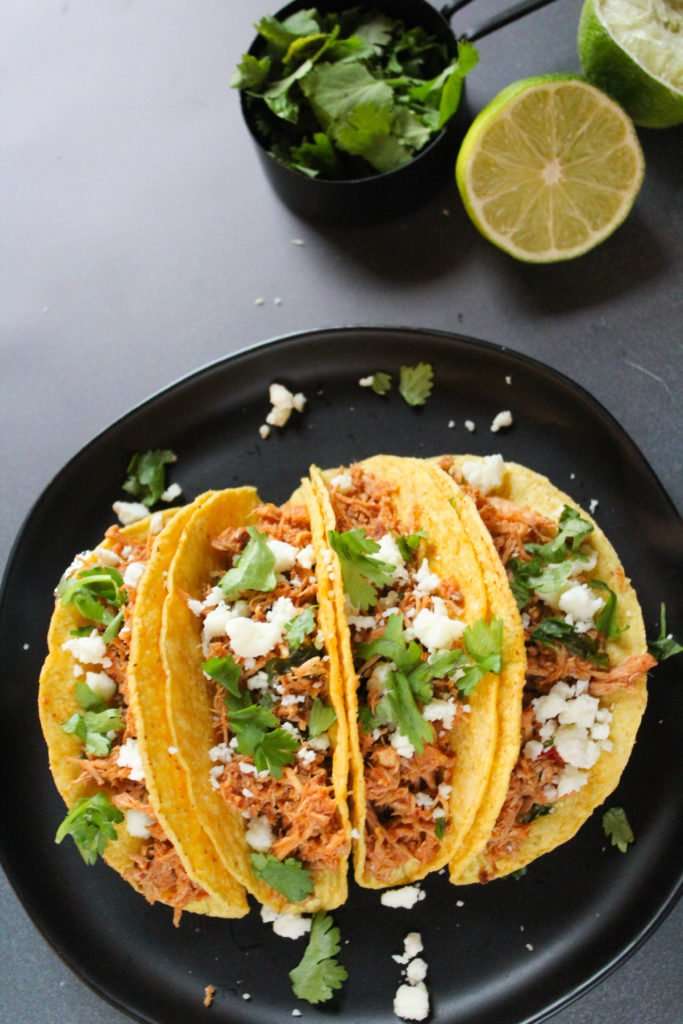 Slow Cooker Chicken Tacos topped with cilantro and cheese , on a black plate.