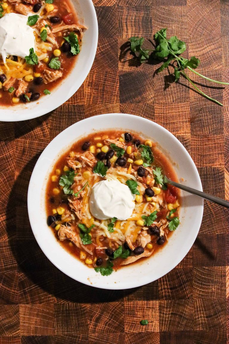 Slow Cooker Chicken Taco Soup topped with cheese and sourcream. on a wooden background.