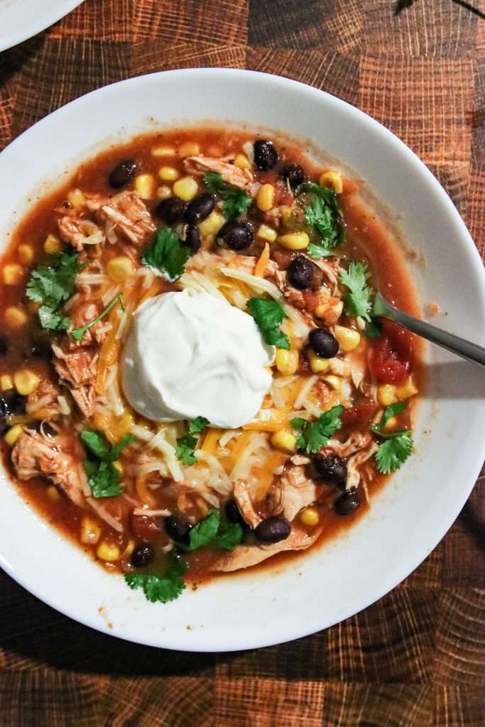 Slow Cooker Chicken Taco Soup topped with cheese and sourcream. on a wooden background.