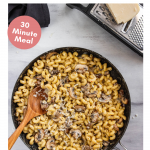 Creamy Skillet Mushroom Mac and Cheese in a skillet. Next to it is a cheese grader with cheese and a napkin.