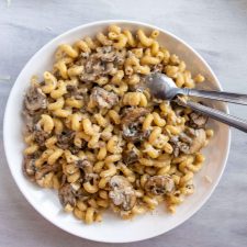 Creamy Skillet Mushroom Mac and Cheese piled on a plate. Next to it is a cheese grader with cheese and a napkin.