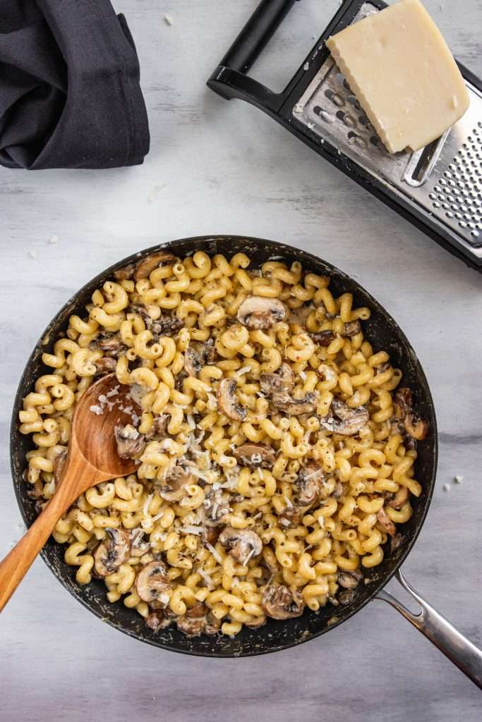 Creamy Skillet Mushroom Mac and Cheese piled on a plate. Next to it is a cheese grader with cheese and a napkin. 