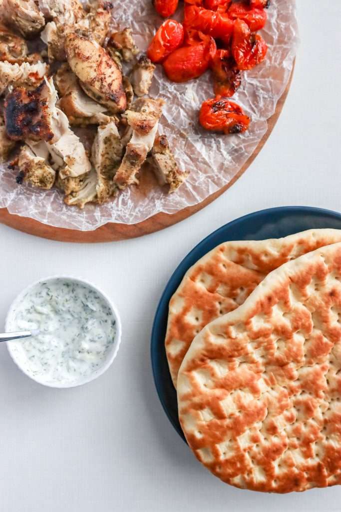 Greek Chicken Pita with Yogurt Sauce on a blue plate with pita and chicken / tomatoes around