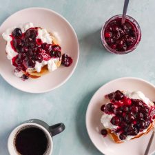 Pancakes topped with whipped cream and Berry Sauce. Next to a jar of berry sauce and a coffee mug