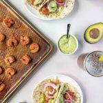 Easy Shrimp Tacos on a Sheet Pan next to tacos on a plate and a small bowl of avocado cream sauce