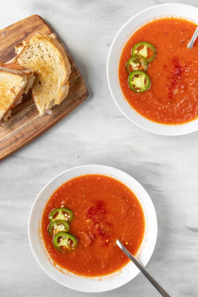 Spicy Tomato Soup with jalapenos on top and a sandwich nearby.
