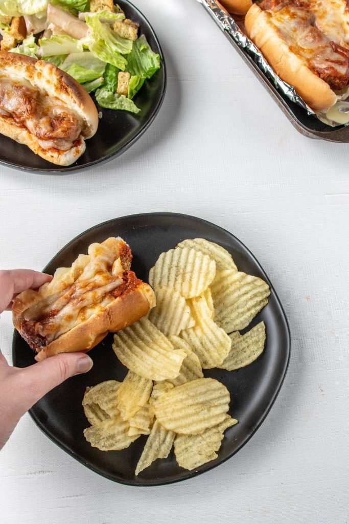 Meatball sub on a plate with chips.