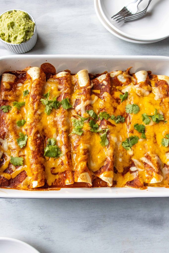 Shredded Pork Enchiladas in a baking dish with cheese on top.