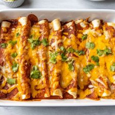 Shredded Pork Enchiladas in a baking dish with cheese on top.