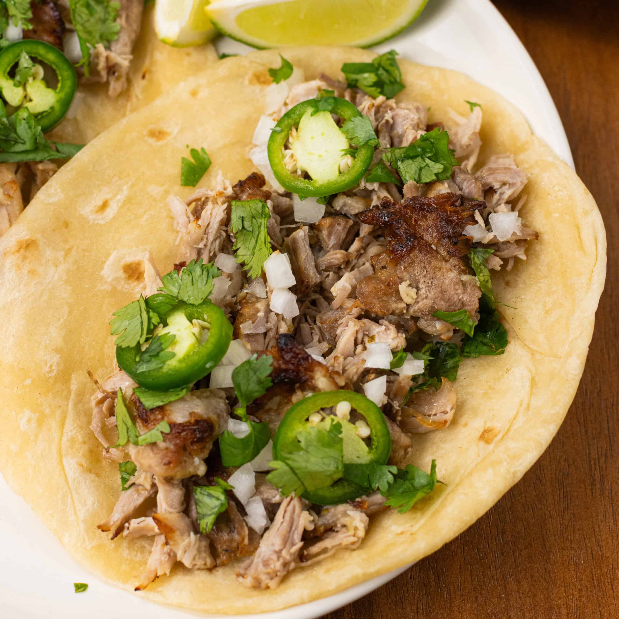 Juicy pork carnitas in a taco with a tortilla, jalapeño, and cilantro