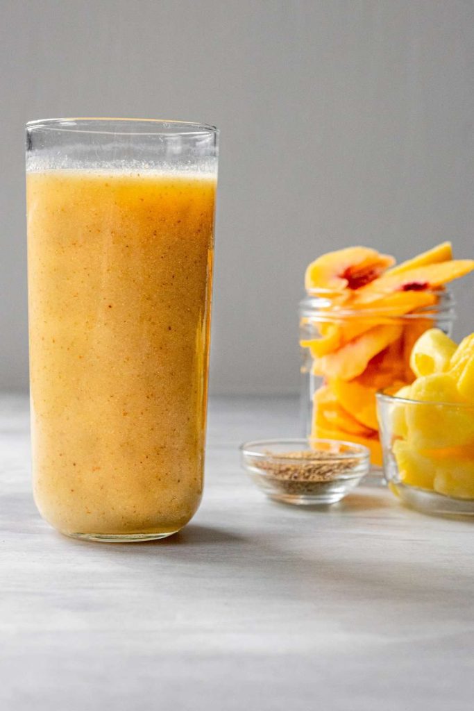 Pineapple Peach Smoothie with frozen pineapples and peaches in the background