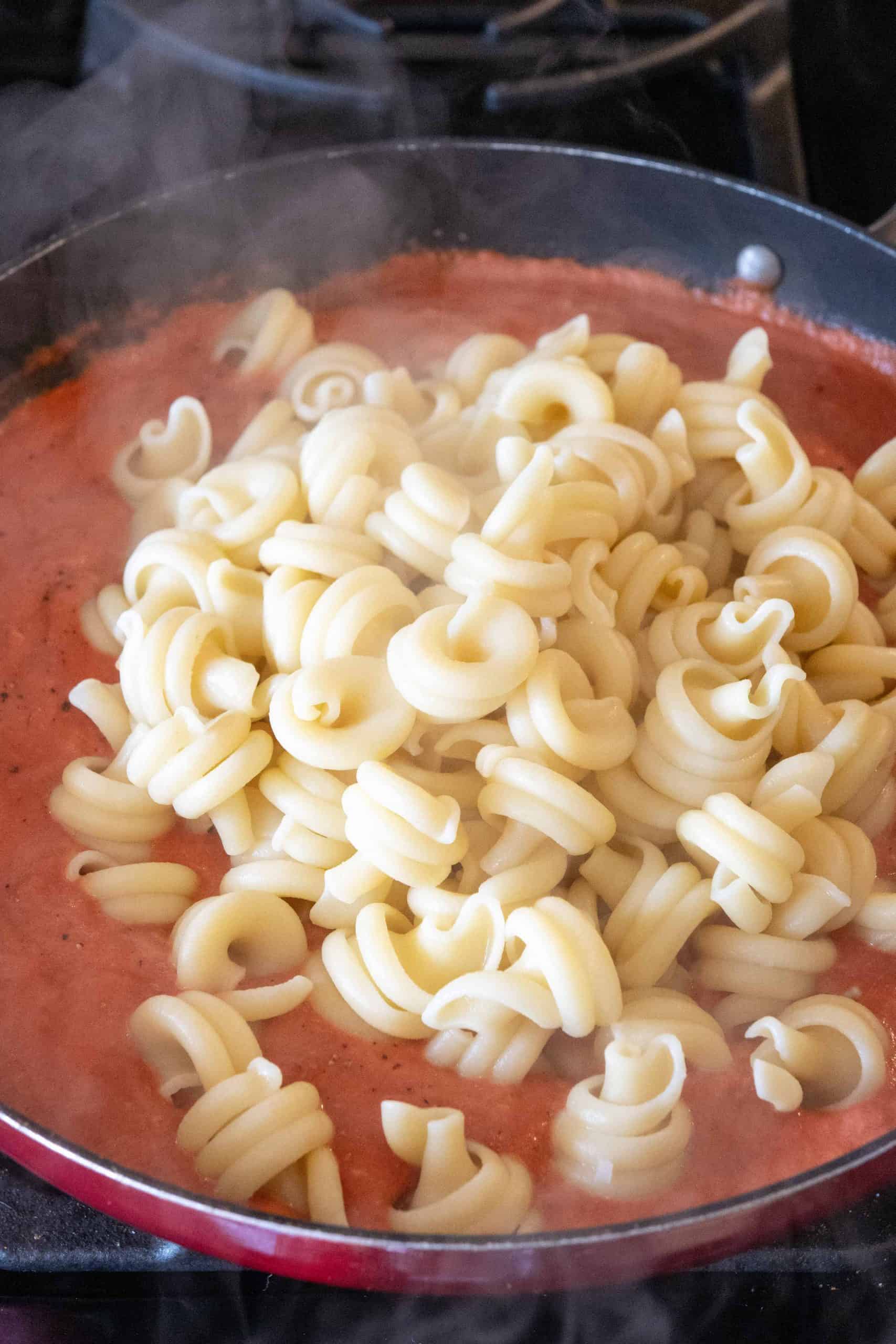 adding pasta to pink sauce