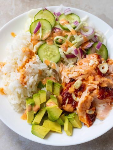 Rice, salmon, avocado and pickled vegetables in a bowl, covered in spicy mayo.