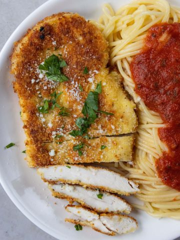 cut up Crusted Chicken Romano next to spaghetti