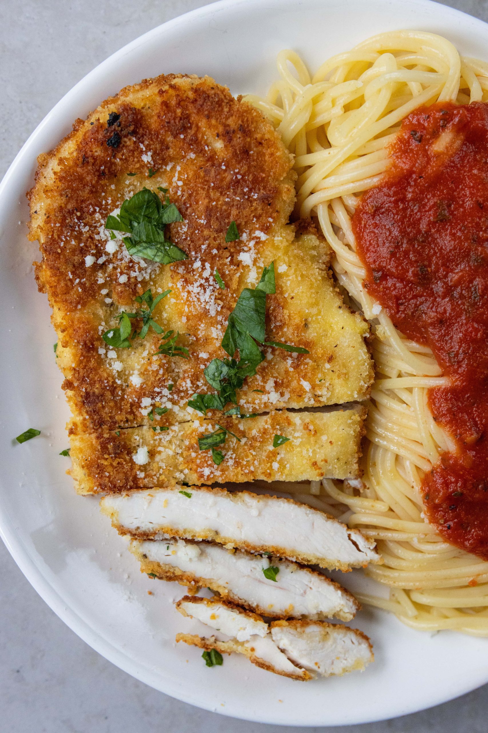 cut up Crusted Chicken Romano next to spaghetti 