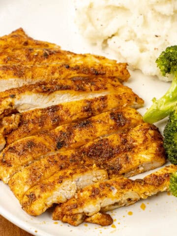 baked thin chicken breast on a plate with broccoli and mashed potatoes
