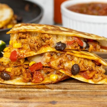 Ground Turkey Quesadillas on a wooden board with salsa behind it