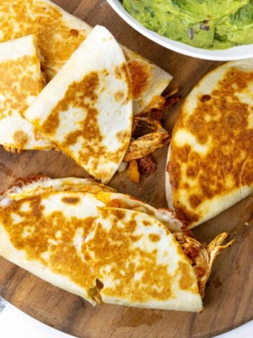 chicken quesadillas on a wooden board with green sauce net to them