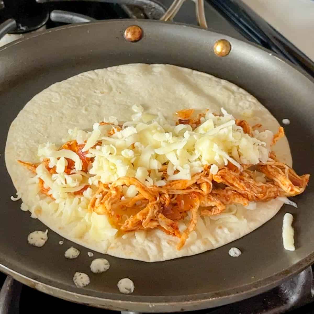 chicken and cheese on a tortilla in a skillet