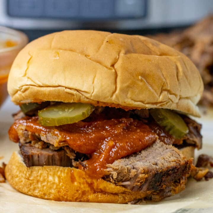 bbq brisket sandwich with bbq sauce and pickles on it. there is a slow cooker in the background