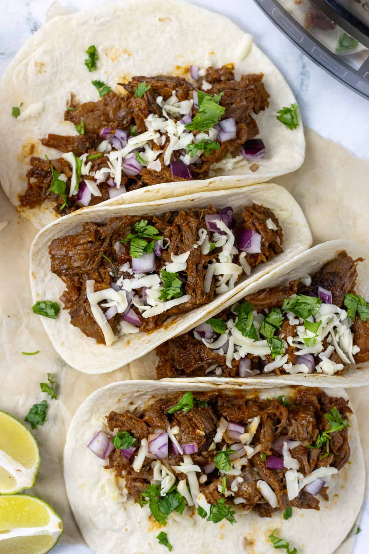 beef brisket tacos with onions, cilantro and cheese next to a lime and slow cooker