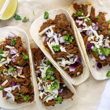 beef brisket tacos with onions, cilantro and cheese next to a lime and slow cooker