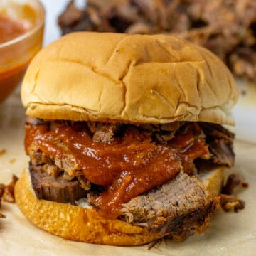 bbq brisket sandwich with bbq sauce and pickles on it. there is a more brisket in the background