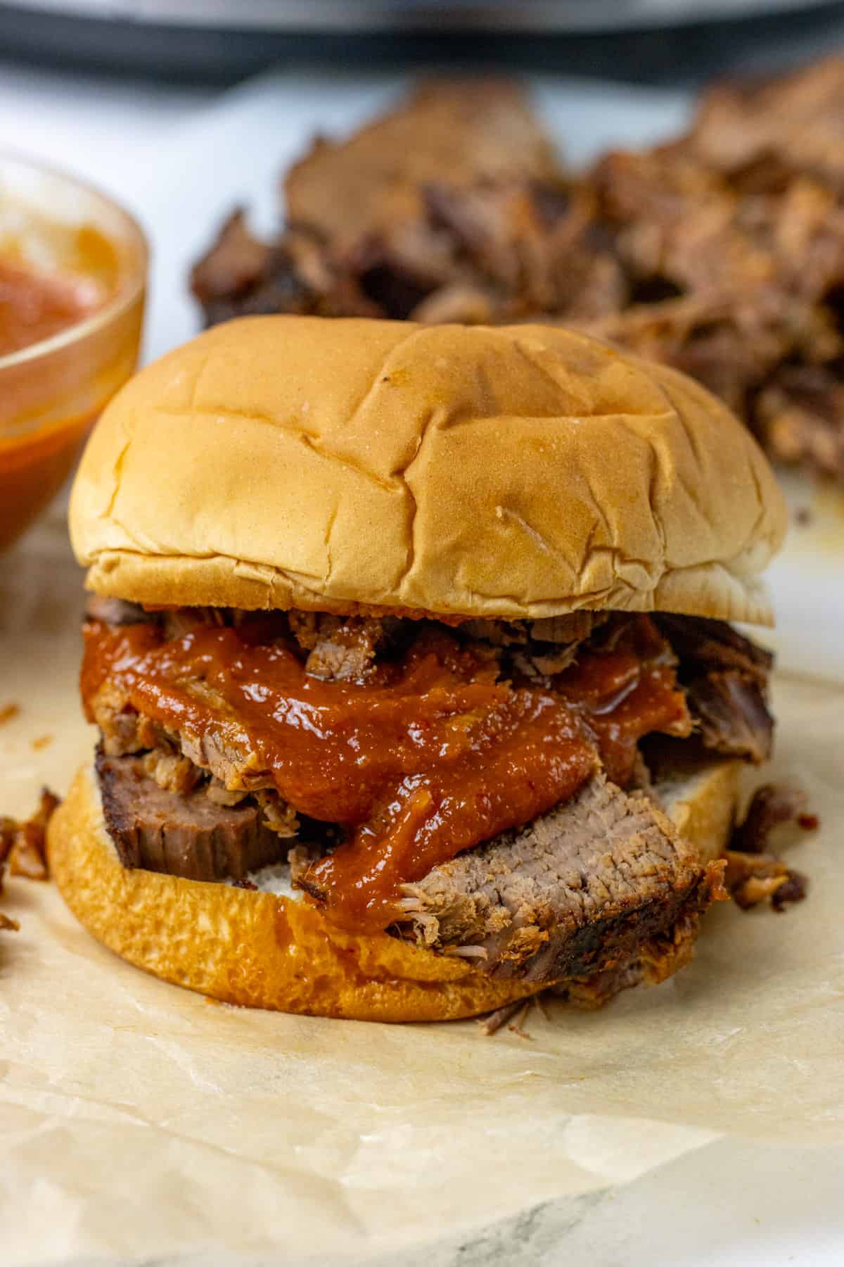 bbq brisket sandwich with bbq sauce and pickles on it. there is a more brisket in the background 