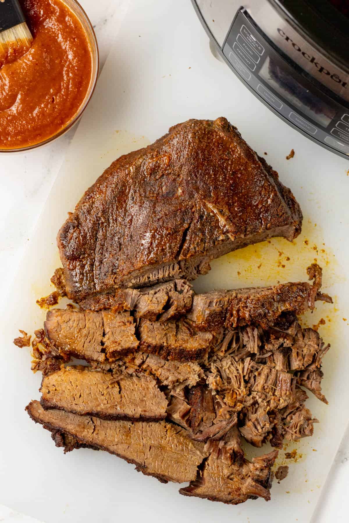 sliced BBQ beef brisket with bbq sauce and slow cooker next to it