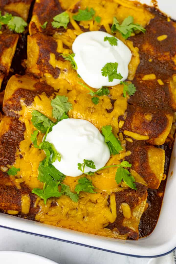 Corn tortilla enchiladas with cilantro and sour ream on top and a spatula scooping it out