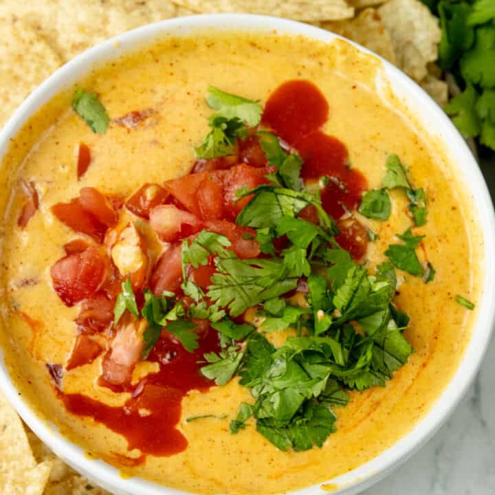 queso topped with hot sauce, tomatoes, and cilantro