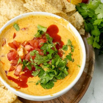 queso topped with hot sauce, tomatoes, and cilantro