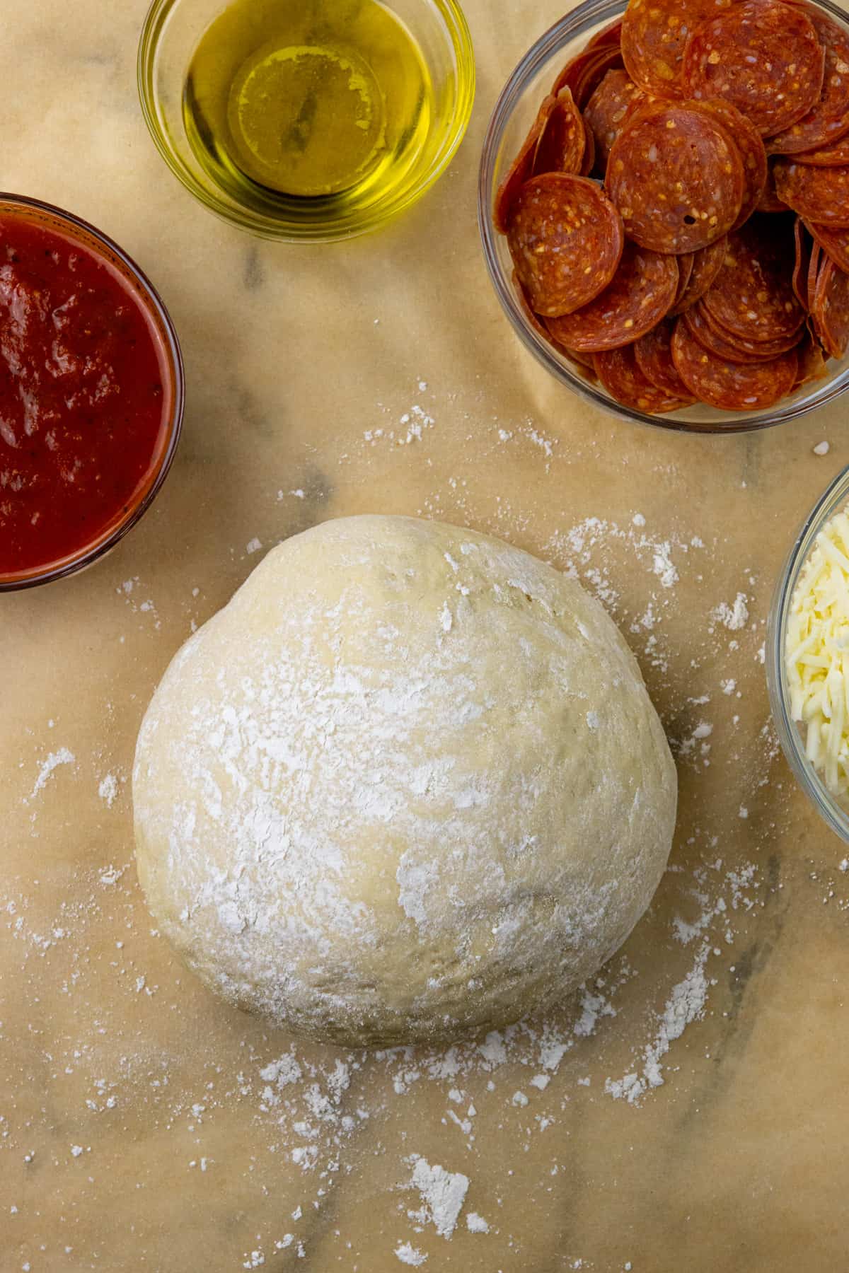 raw pizza dough with pizza toppings round it 