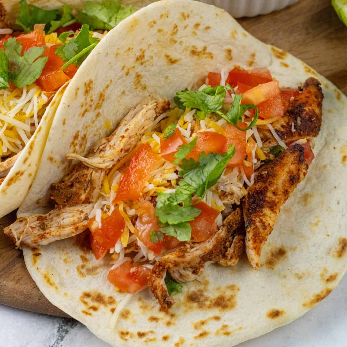 chicken tacos with cheese, tomatoes, and cilantro