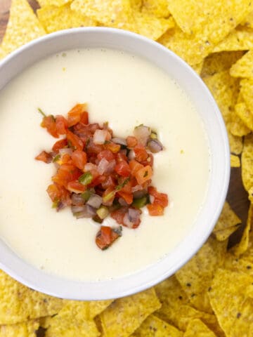 white queso with pico de gallo topping it. Chip surrounding the queso.