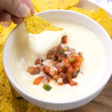 white queso with pico de gallo topping it. Chip dipping into queso.