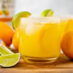 Texas Margarita in a cup with a lime wedges and ingredients all around