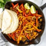 Fajita veggies in a cast iron skillet with tortillas