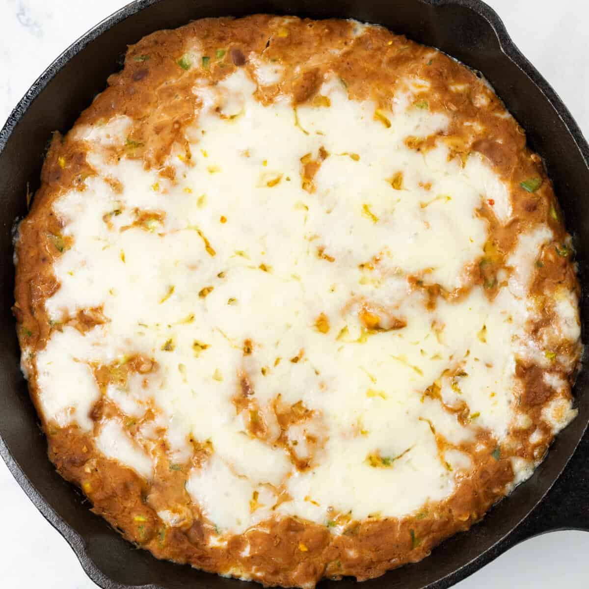Spicy Refried Bean Dip with melted cheese in cast iron