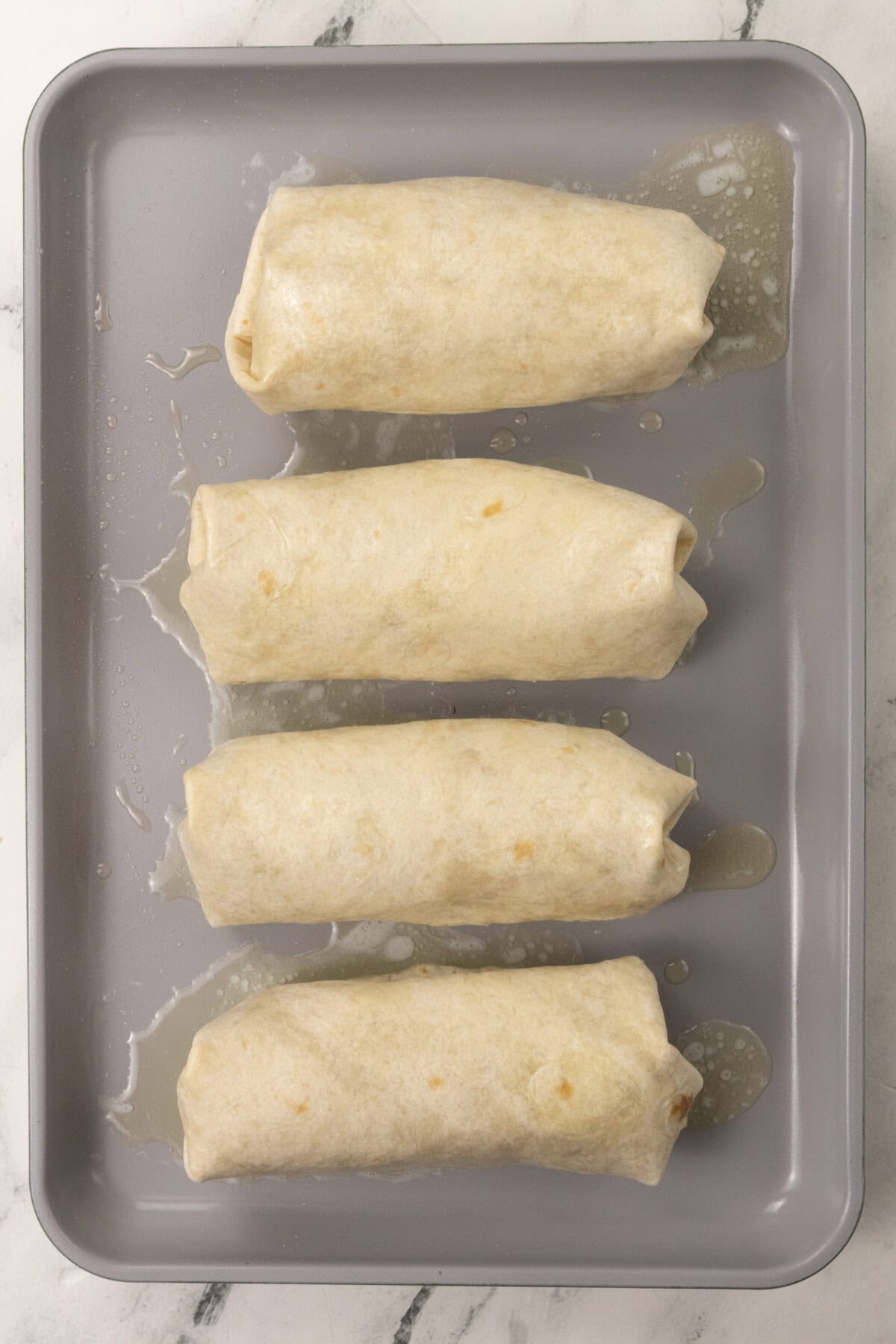 fully formed chimichangas with butter on pan ready to be baked