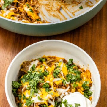 shot of finished 30 Minute One Pan Beef Enchilada Skillet in a bowl with the pan with more of the recipe in the background