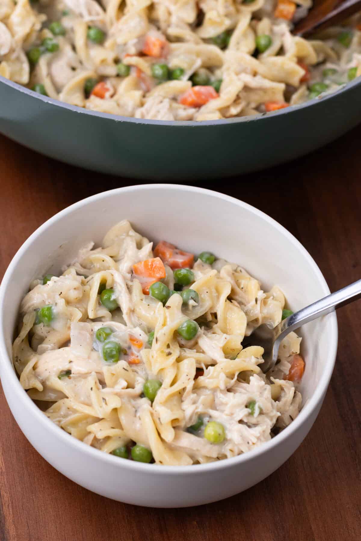 finished bowl of chicken noodle pasta with pan of food in the background
