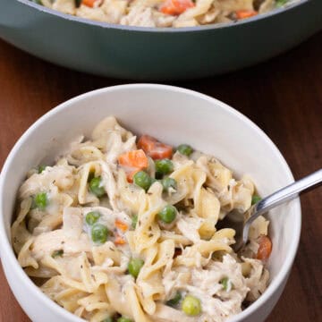 finished bowl of chicken noodle pasta with pan of food in the background