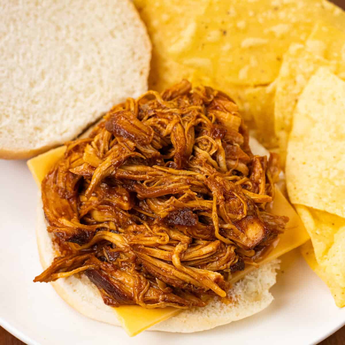 close up of finished Slow Cooker BBQ Chicken on a bun with chips and cheese ready to serve