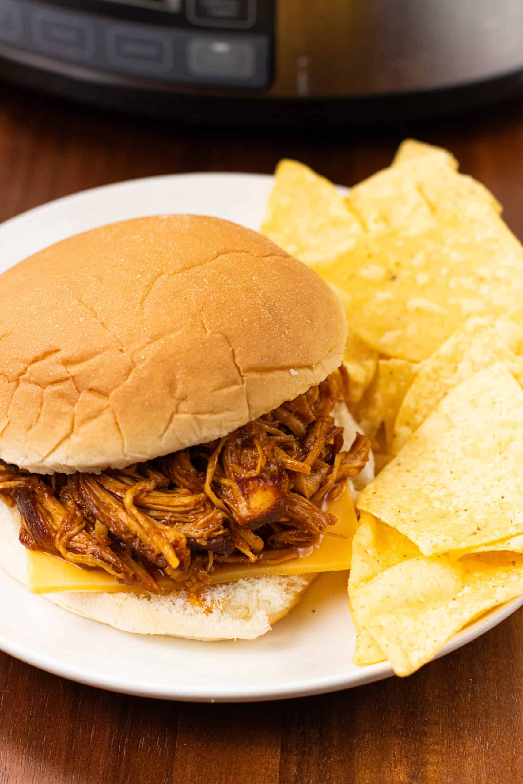 finished Slow Cooker BBQ Chicken in a bun with cheese and chips