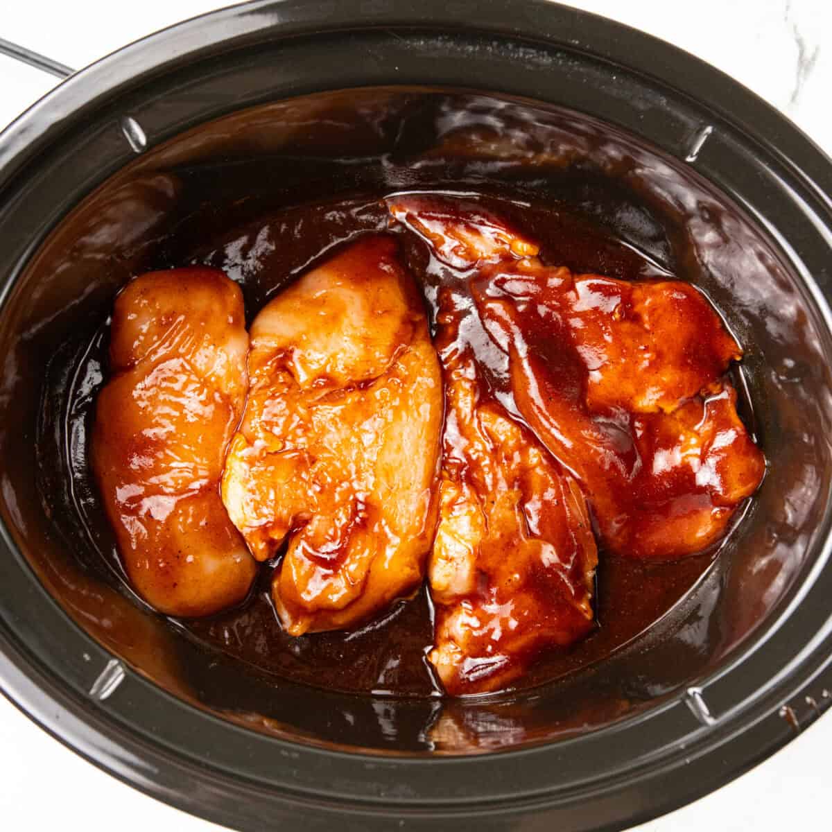 bbq and raw chicken sitting in crockpot for Slow Cooker BBQ Chicken recipe